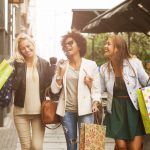 Three attractive young girls holding shopping bags while walking on the street laughing and smiling in downtown Baltimore