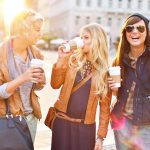 Young friends together walking in the city, talking and drinking coffee from paper cup.